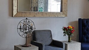 A room with two blue upholstered chairs, a small table with a decorative metal lamp, and a vase with flowers.