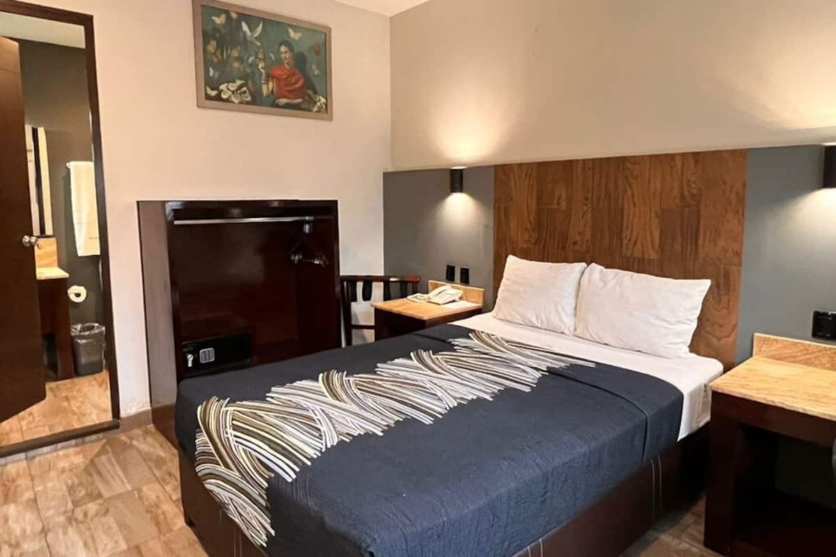 Una habitación de hotel con una cama, cabecera de madera, mesita de noche, escritorio y una puerta.