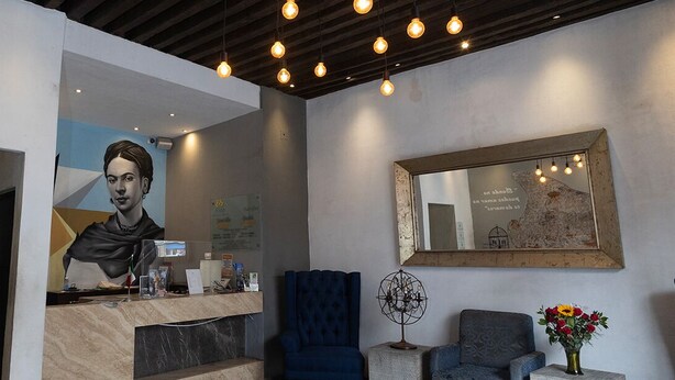A reception area with a marble counter, a blue upholstered chair, a small table with a decorative item, and a mirror on the wall.