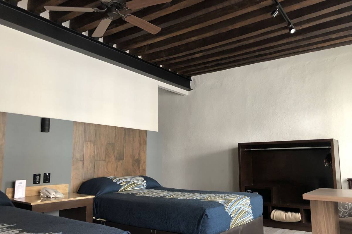 Habitación de hotel con dos camas, un escritorio, un teléfono, un televisor y un ventilador de techo.