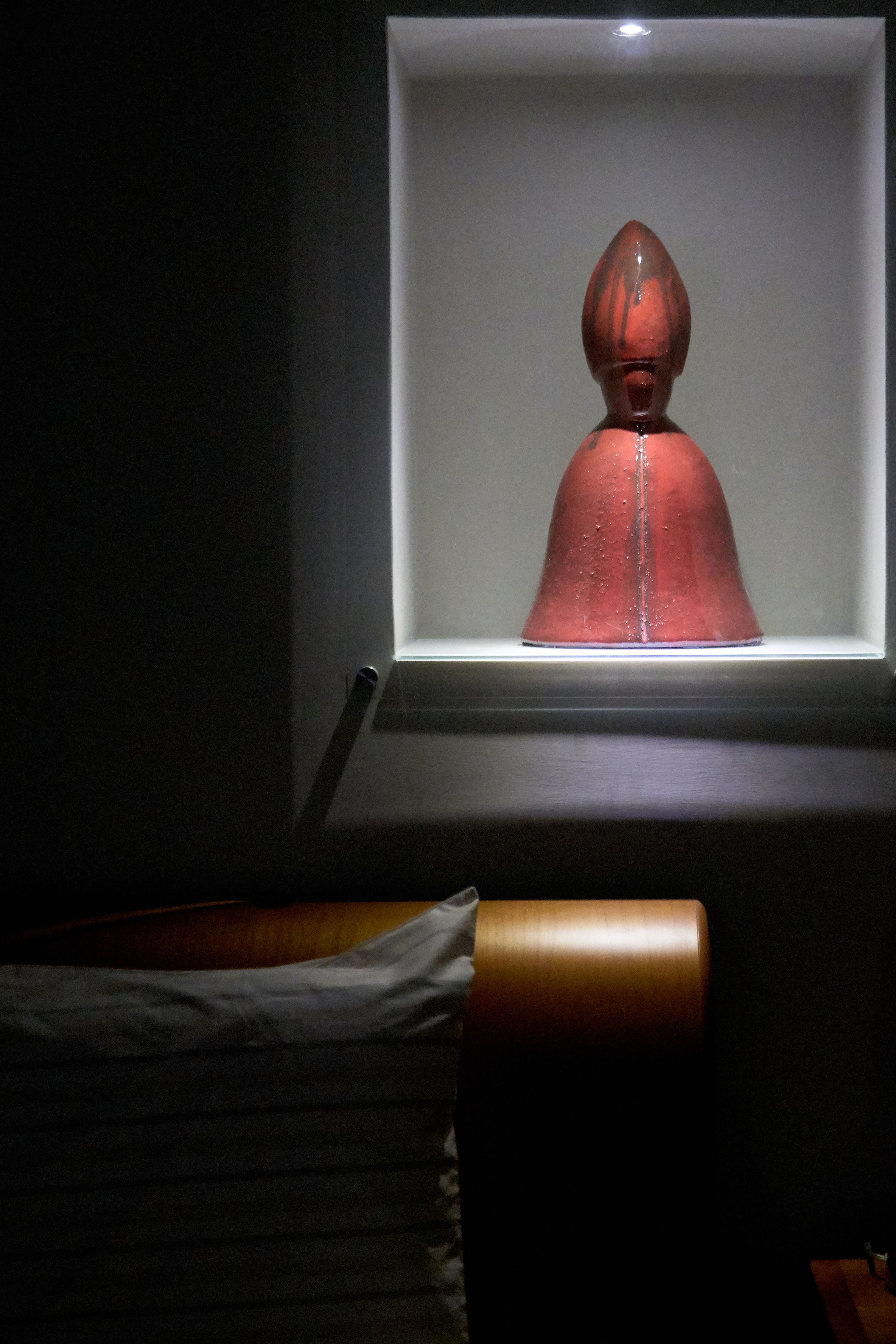 A room with a bed, a window, and a sculpture.