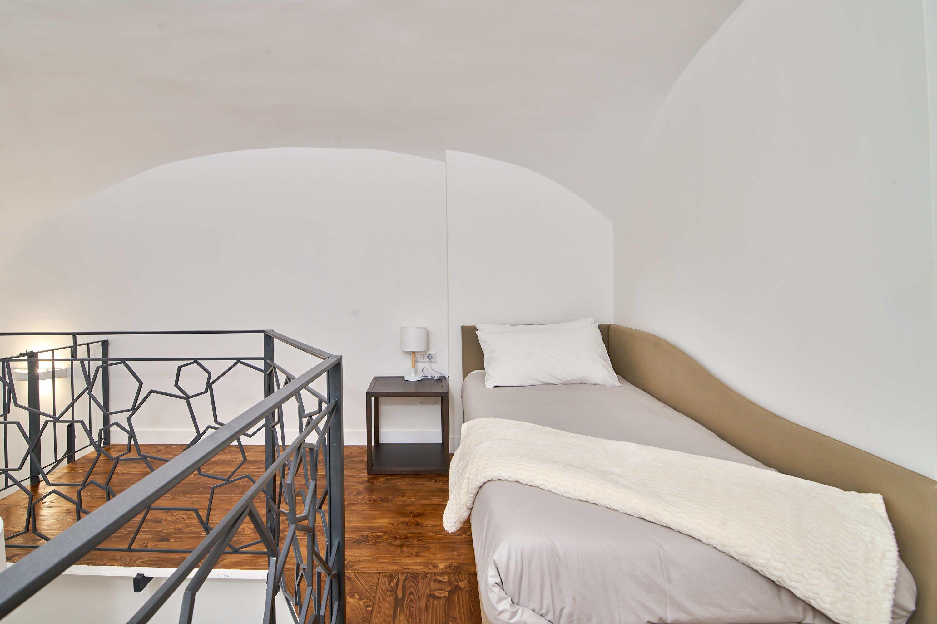 Une chambre à coucher avec un lit, une table de chevet, une lampe et une balustrade aux motifs géométriques.