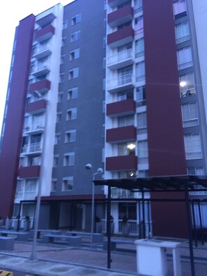 A multi-story residential building with balconies, a covered outdoor seating area, and a street in front. - Apartamento Granate (Pereira)