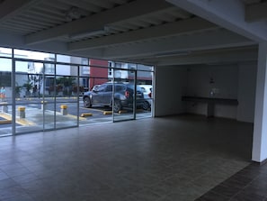 A parking garage interior with a glass wall, a tiled floor, and a visible car outside. - Apartamento Granate (Pereira)