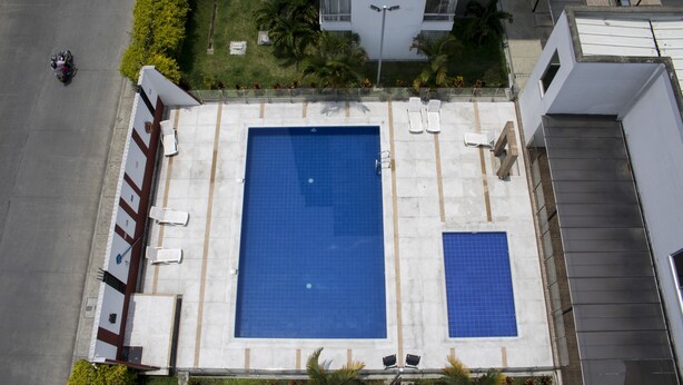 An aerial view of a swimming pool with a tiled deck, surrounded by a low wall and a few lounge chairs. - Apartamento Granate (Pereira)