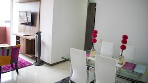 A modern dining area with a glass table, white chairs, and a pink rug. - Apartamento Granate (Pereira)