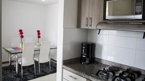 A modern kitchen with a microwave, coffee maker, and gas stove. There is a dining area with a glass table and white chairs. - Apartamento Granate (Pereira)