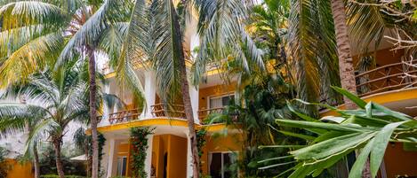Un patio de hotel con palmeras, un edificio amarillo y un césped bien cuidado.