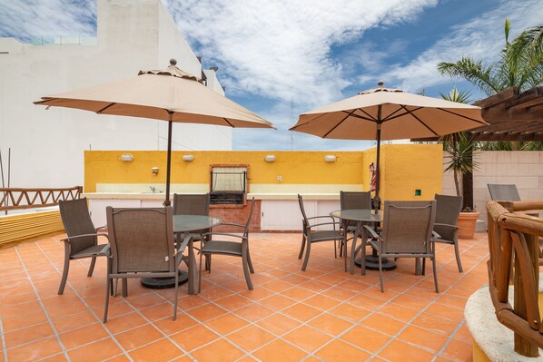 A rooftop patio with outdoor seating, including tables and chairs, and large umbrellas.