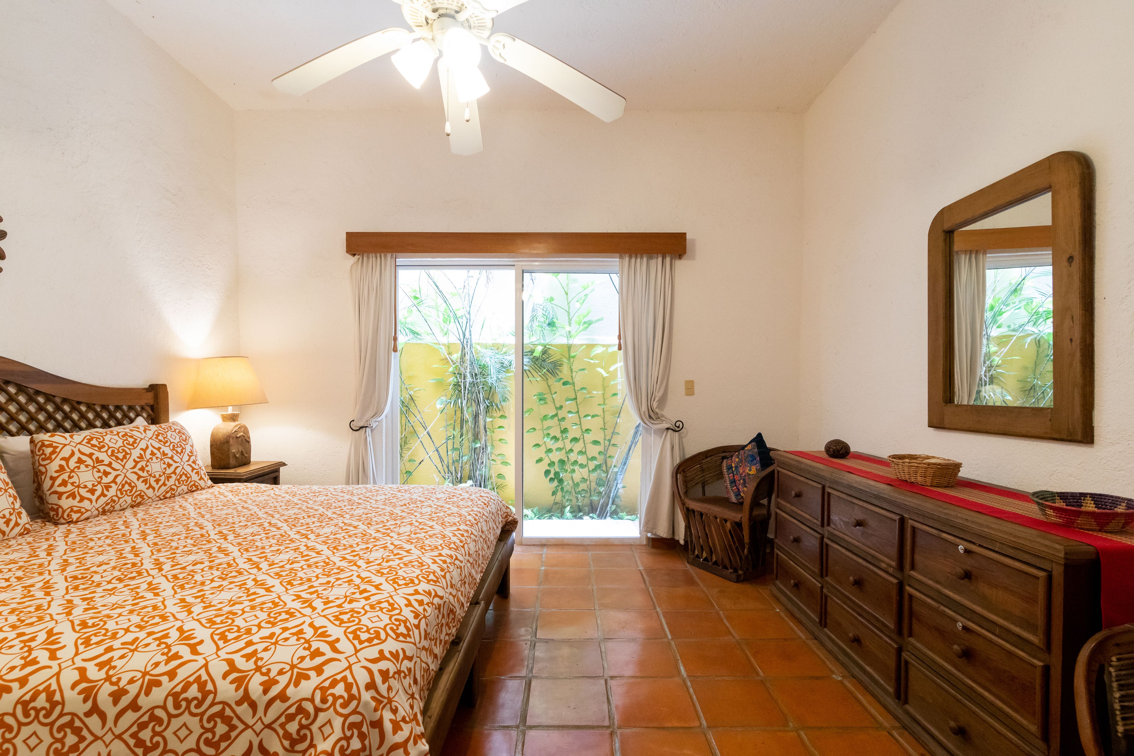 Une chambre à coucher comprenant un lit, une table de chevet, une commode, un miroir et une porte-fenêtre coulissante donnant sur un balcon.
