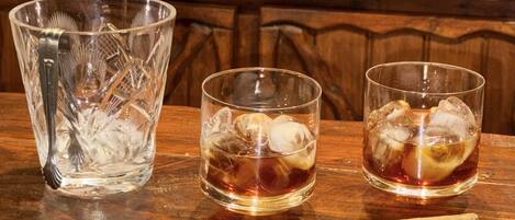 A bar setting with a glass pitcher, two glasses with ice cubes, and a cigar on a wooden surface.