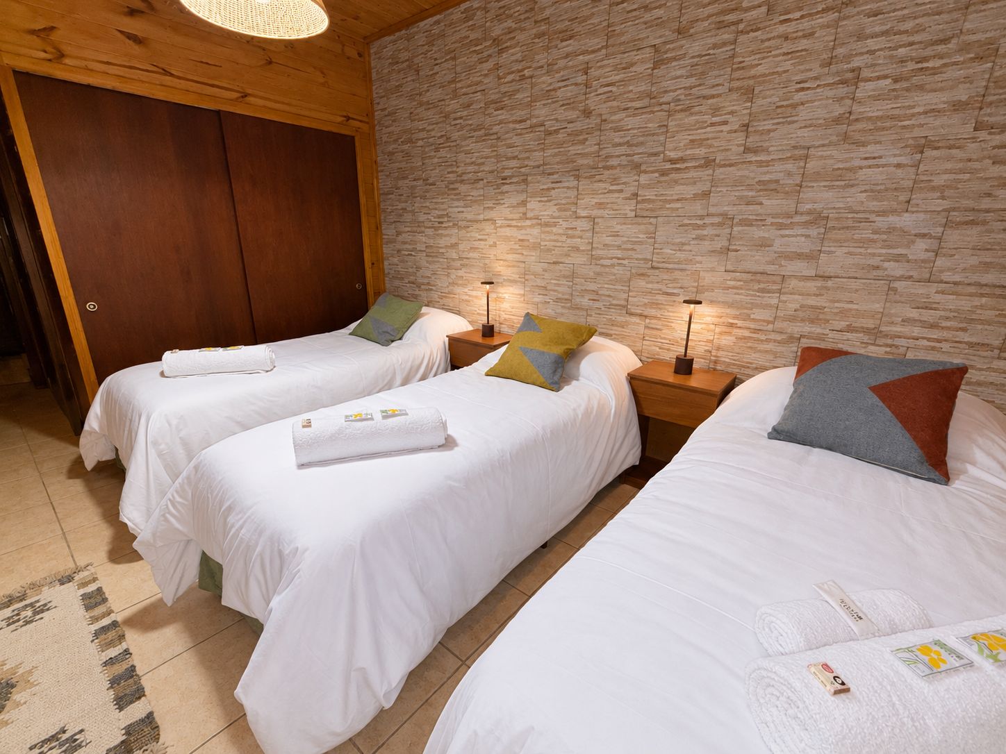Ein Hotelzimmer mit drei Einzelbetten, Holzboden, einer Steinwand und einem Schrank aus Holz.