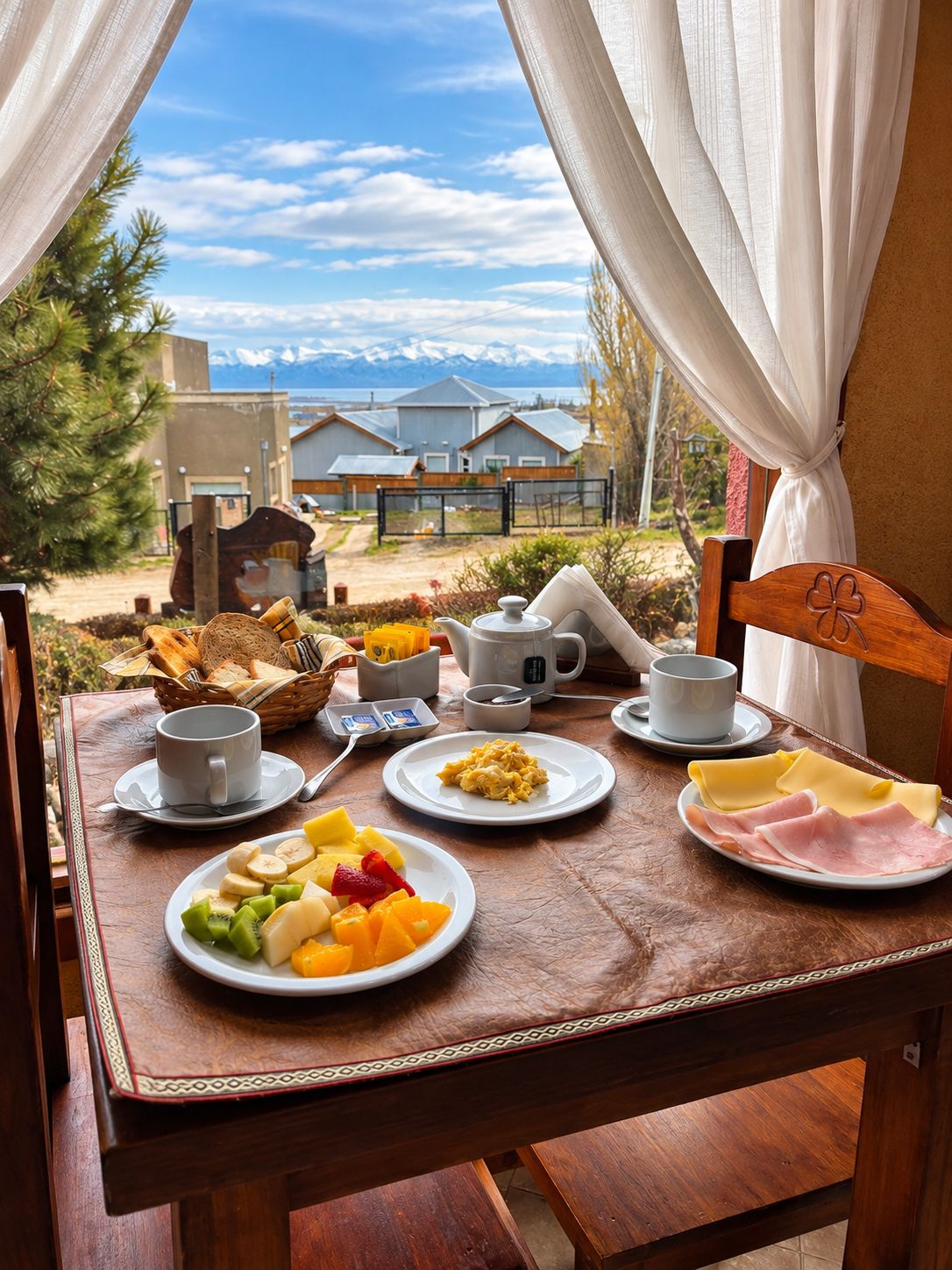 Ein Esstisch mit Speisen, Tassen und Blick auf Häuser und Berge.