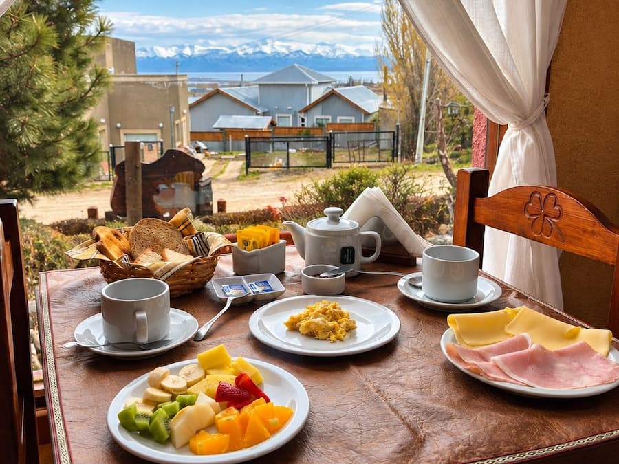 A breakfast table with plates of food, cups, and a view of houses and mountains.