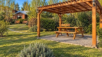A wooden pergola with a picnic table, surrounded by a well-maintained garden with a lawn and gravel path.