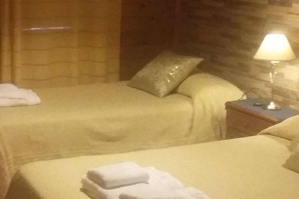 A hotel room with two beds, a nightstand with a lamp, and a window with curtains.