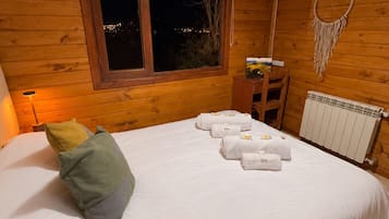 Una habitación de madera con una cama, una ventana, un atrapasueños colgado en la pared y un radiador.