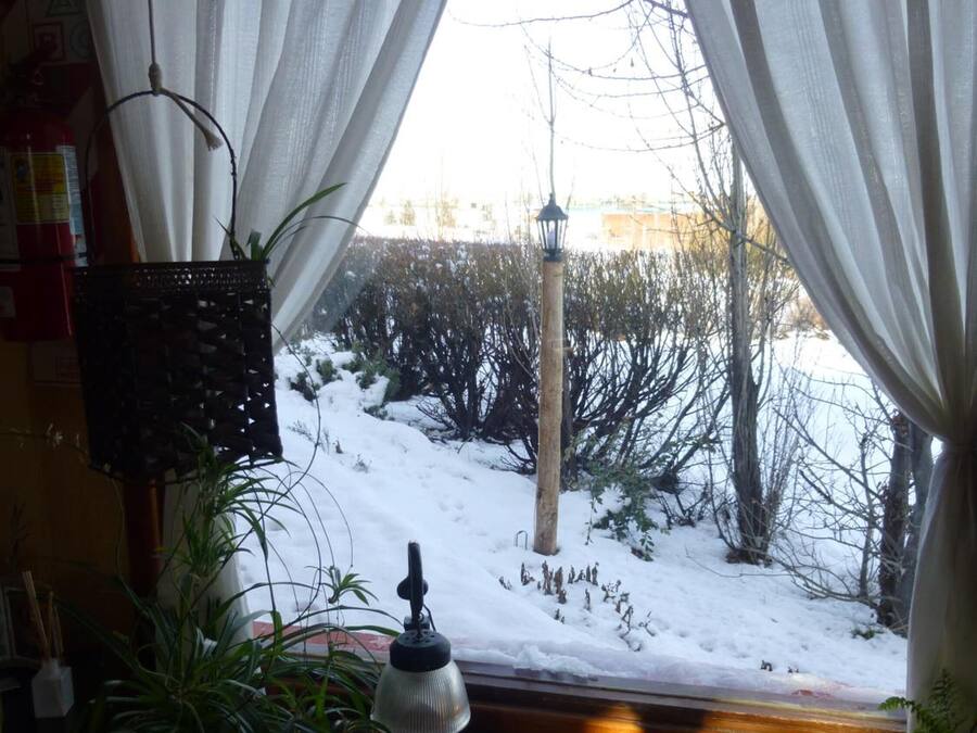 A room with a window overlooking a snowy landscape, a table with decorative items, and a hanging lamp.