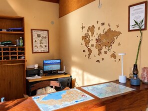 Quarto com escrivaninha de madeira, computador, mapas e um mapa de parede.