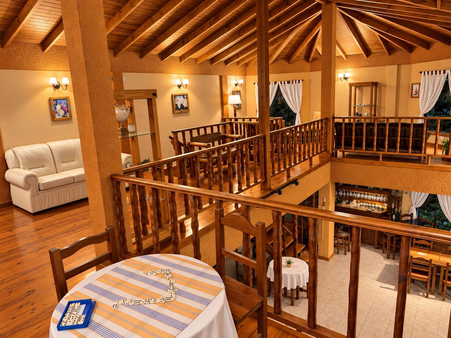 A hotel room with a wooden ceiling, a dining area with a table set for two, and a balcony with a railing.