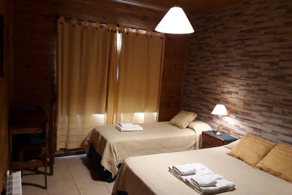 A room with two beds, a wooden desk, a chair, a lamp, and a curtain.
