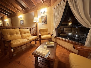 A cozy room with wooden furniture, a table with books, and a window with curtains. - Hosteria Rukahue (El Calafate)