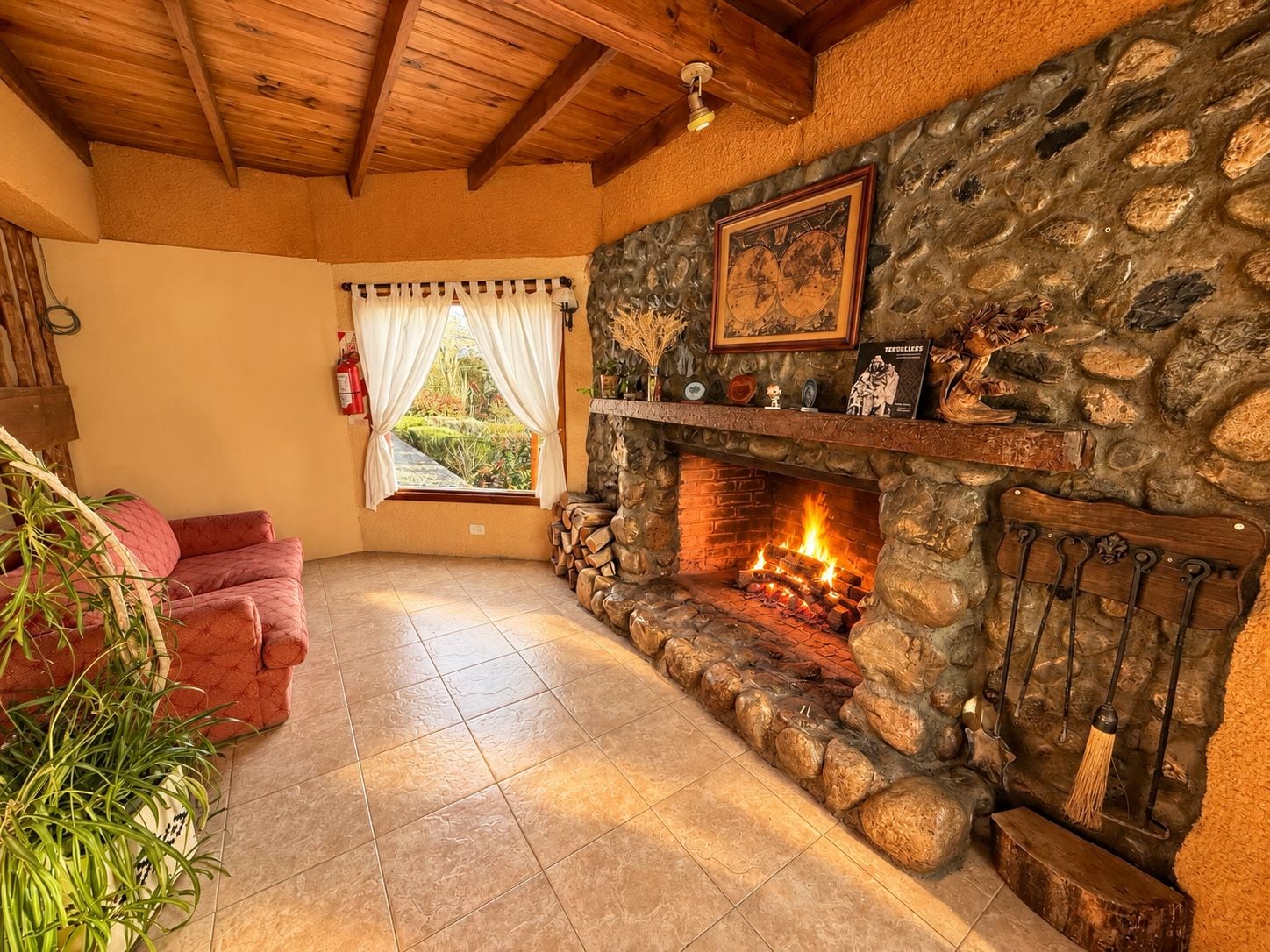 A cozy room with a stone fireplace, a red sofa, and a window with curtains.