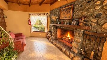 A cozy room with a stone fireplace, a red sofa, and a window with curtains.