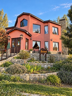 A two-story building with a stone facade, a sign reading 'Ro Kahue,' and a stone staircase leading to the entrance. - Hosteria Rukahue (El Calafate)