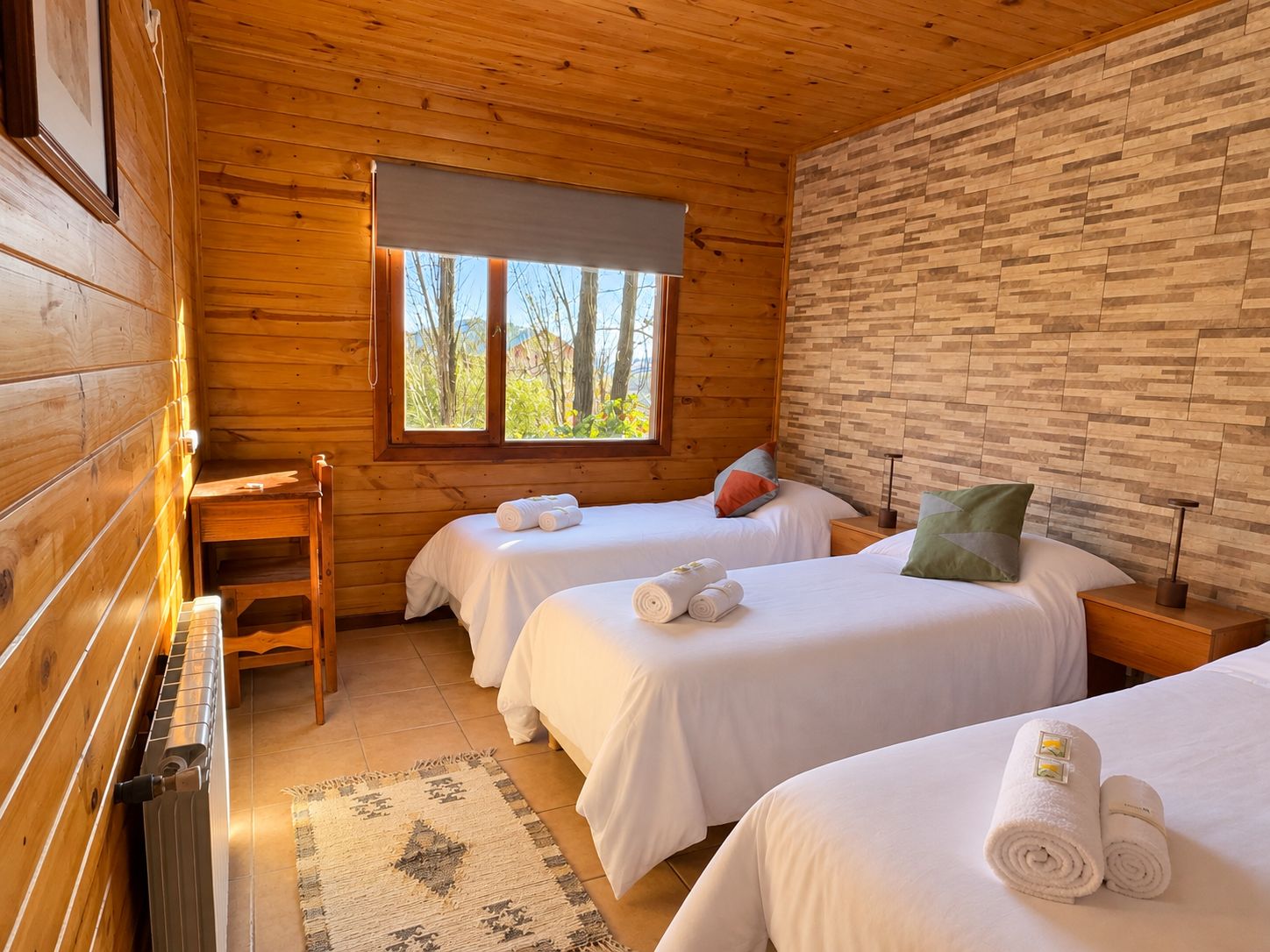 Habitación tipo cabaña con dos camas, ventana con vista a árboles y pared de madera.