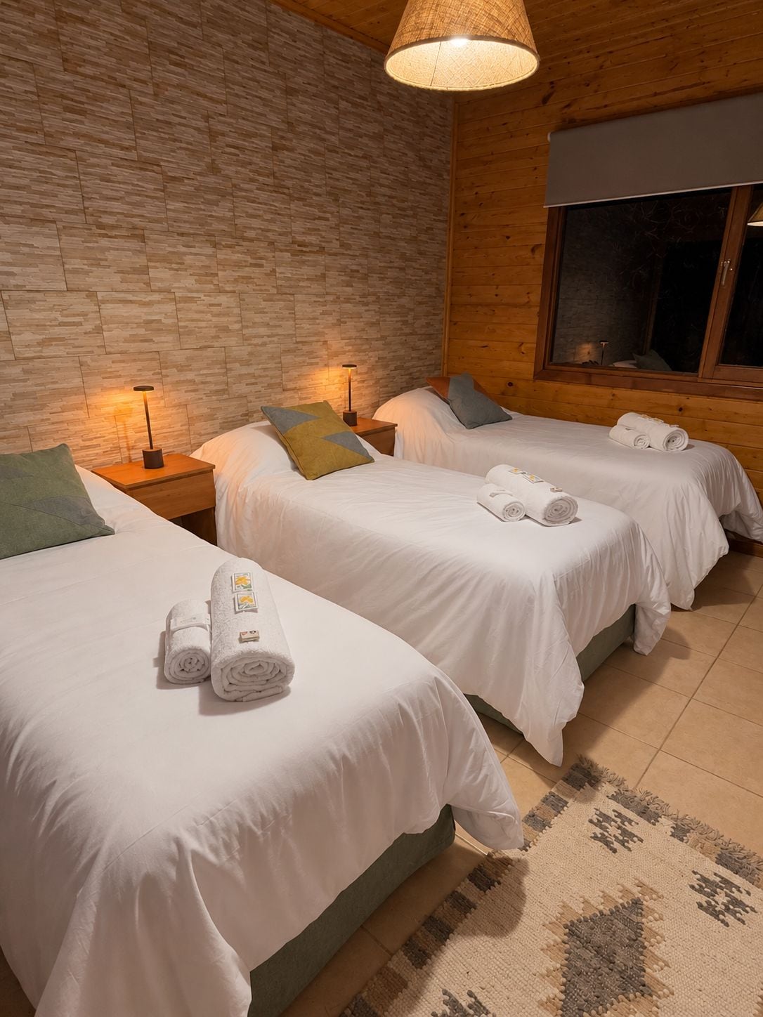 A hotel room with two beds, wooden walls, a large window, and a patterned rug.