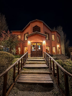 A two-story building with a wooden staircase leading to a set of double doors. - Hosteria Rukahue (El Calafate)