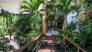 A pathway flanked by lush greenery and a wooden railing, leading to a building entrance. - Via 38 Buda By Playa Paradise (Playa del Carmen)