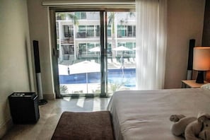 Habitación de hotel con cama, lámpara de noche, una mesita y vista a una piscina y un edificio a través de una puerta de vidrio.