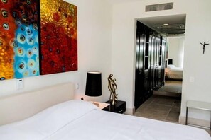 A hotel room with a bed, a nightstand, a lamp, and a colorful abstract painting on the wall.