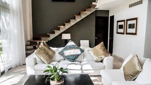 A modern living room with a staircase, white sofas, and a coffee table with a plant. - Via 38 Buda By Playa Paradise (Playa del Carmen)