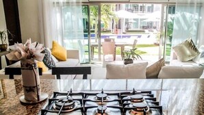 A modern kitchen with a gas stove, a dining area with a table and chairs, and a view of a pool and greenery outside. - Via 38 Buda By Playa Paradise (Playa del Carmen)