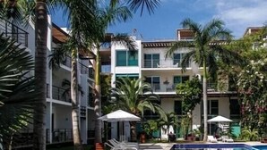 A hotel with a swimming pool, palm trees, and a multi-story building with balconies. - Via 38 Buda By Playa Paradise (Playa del Carmen)