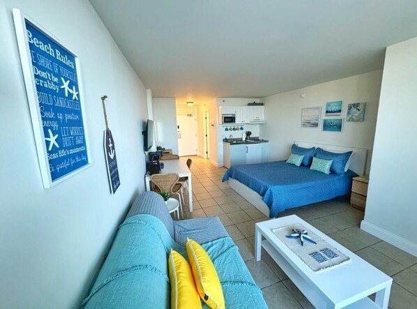 A compact living space with a kitchenette, a dining area, and a bedroom with a bed and a sofa.