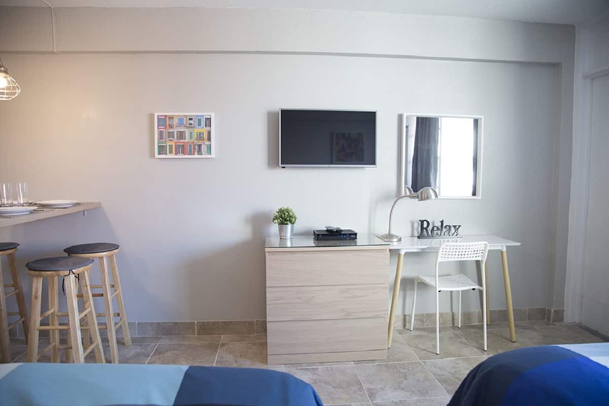 Een moderne kamer met een bureau, twee barkrukken, een stoel, een televisie en een kleine plant.