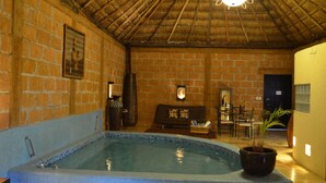 Una habitación con pared de ladrillo, techo de madera, una pequeña piscina, un sofá, una mesa de comedor con sillas y una planta en maceta.