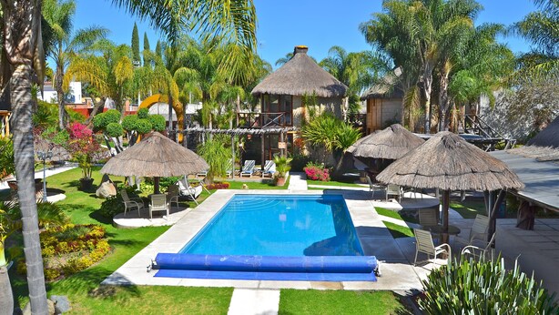 Piscina rodeada de palmeras y construcciones con techo de paja.