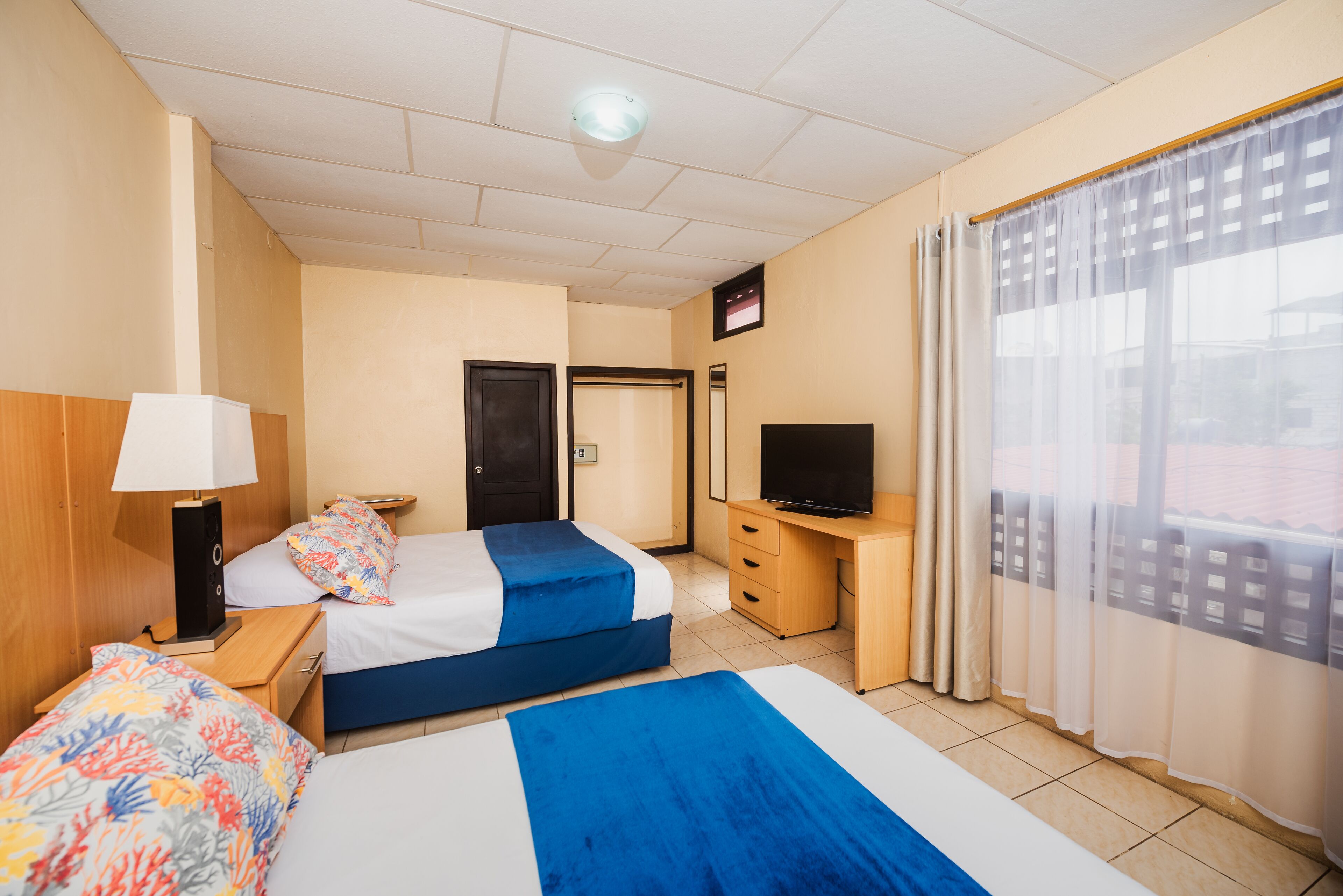 Habitació d'hotel amb dos llits, un escriptori amb televisió, una làmpada i una finestra amb cortines.