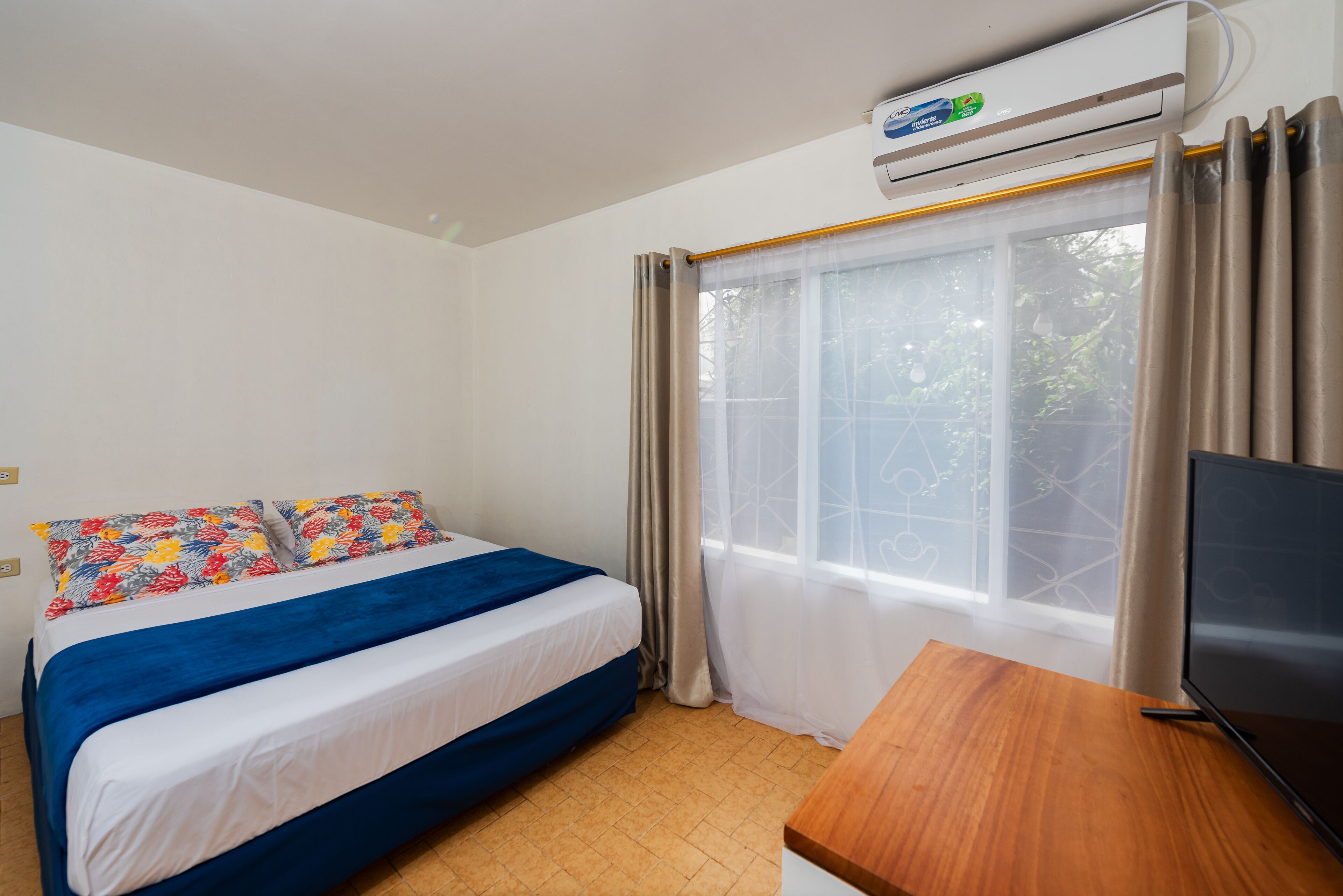 A hotel room with a bed, a wooden desk, a television, and a window with curtains.