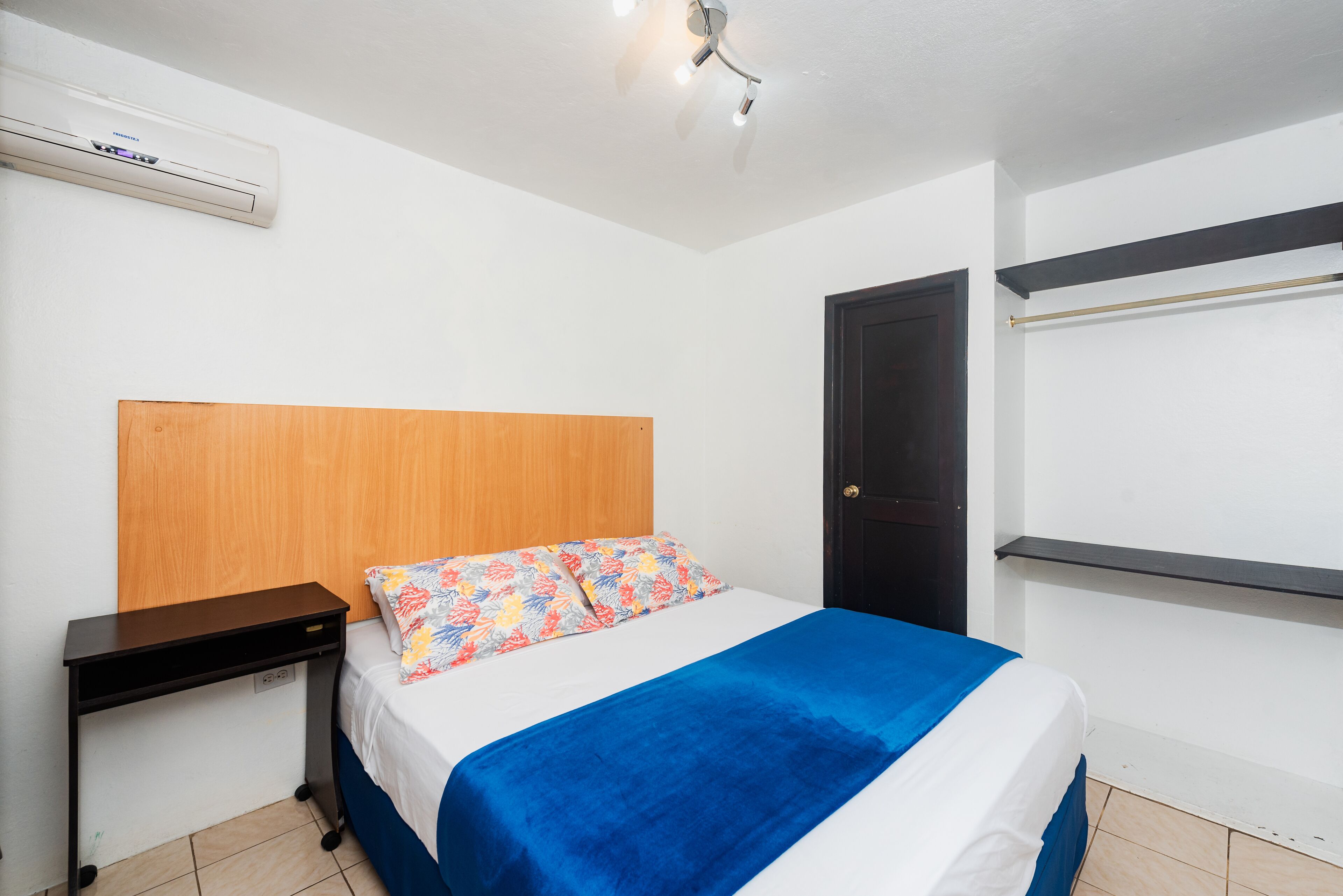 A bedroom with a bed, a nightstand, a wooden headboard, a black door, and a white wall with a mounted air conditioner.