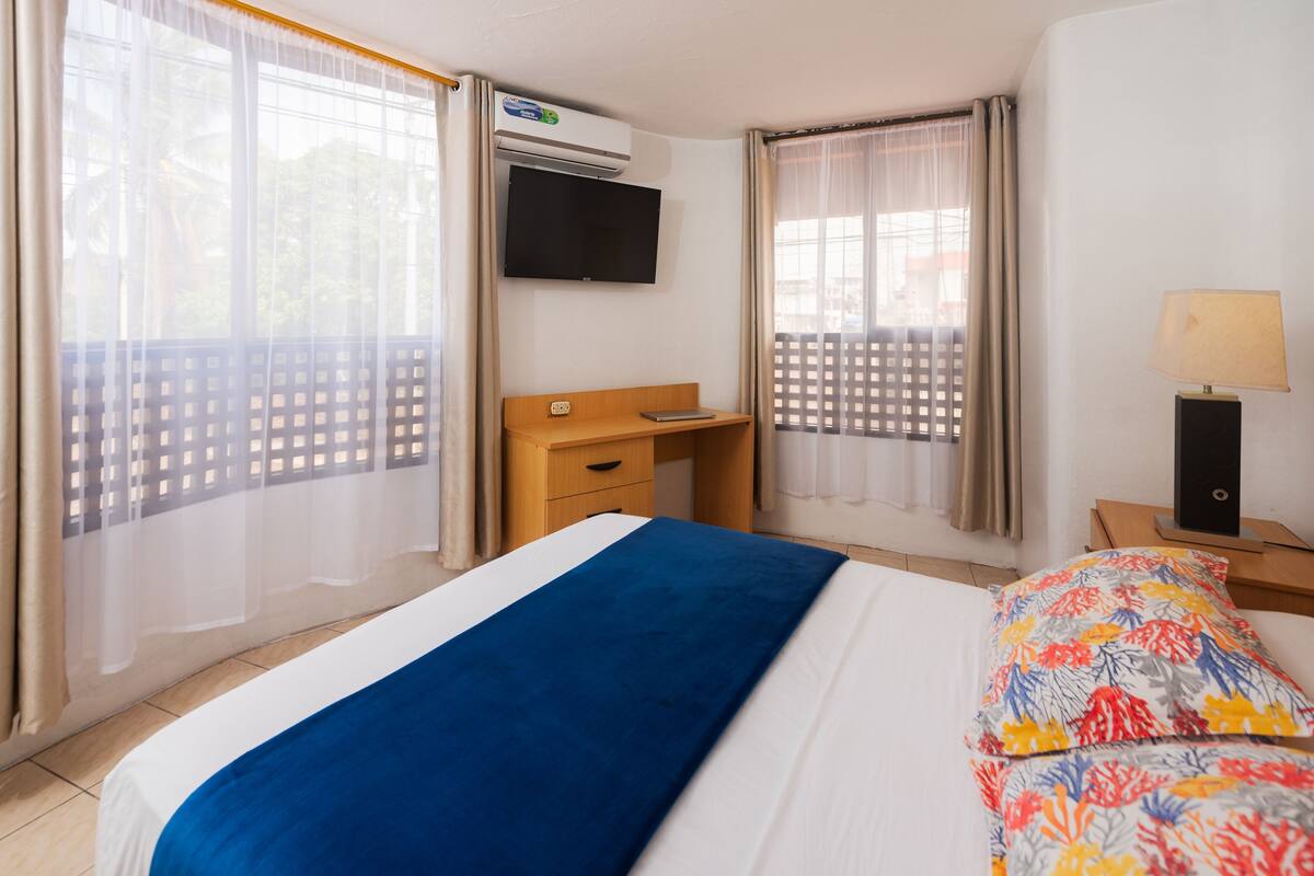 Ein Hotelzimmer mit Bett, Schreibtisch, Fernseher und einem Fenster mit Vorhängen.