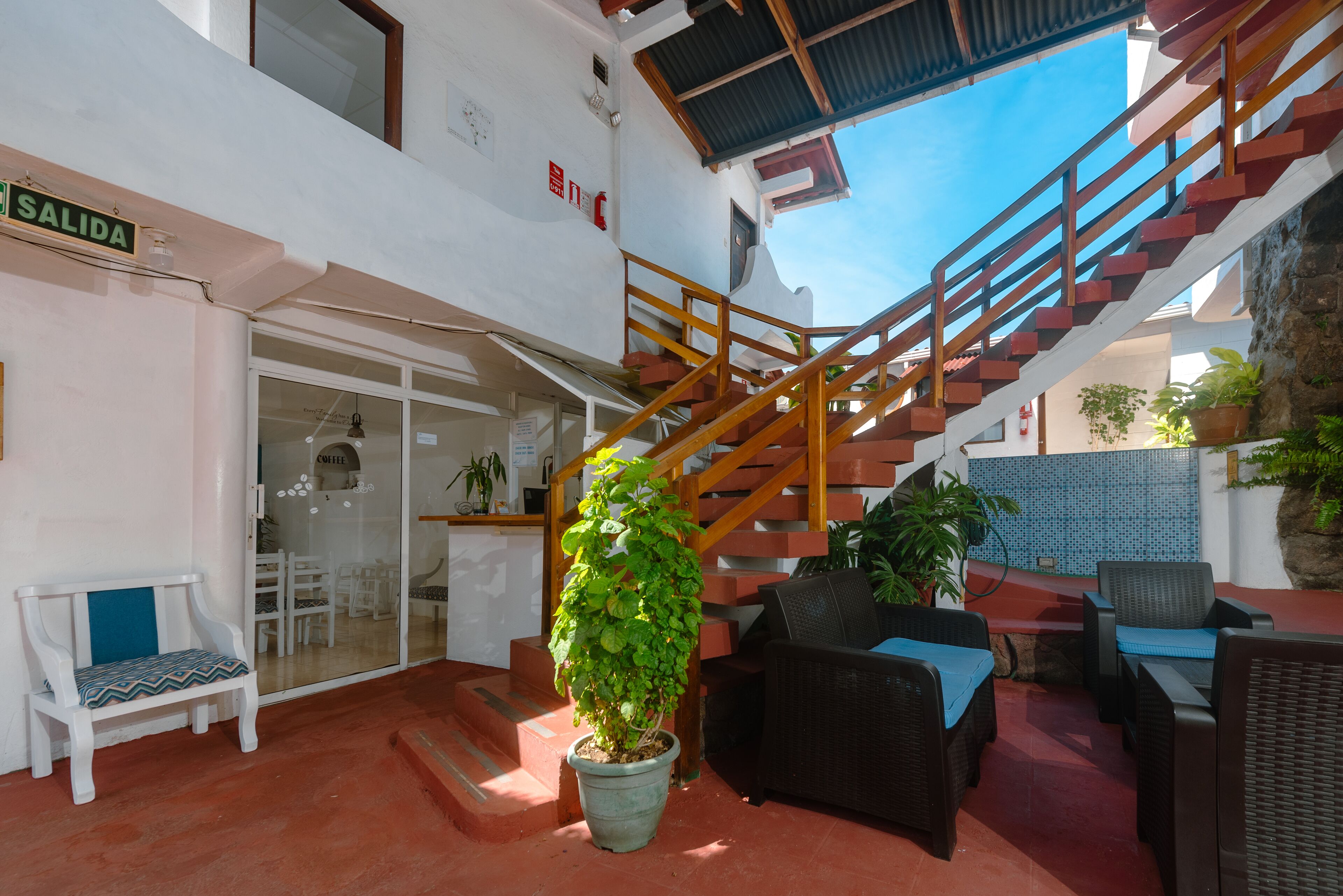 A staircase with wooden railings leading to an upper level, a potted plant, outdoor furniture, and a sign reading "SALIDA".