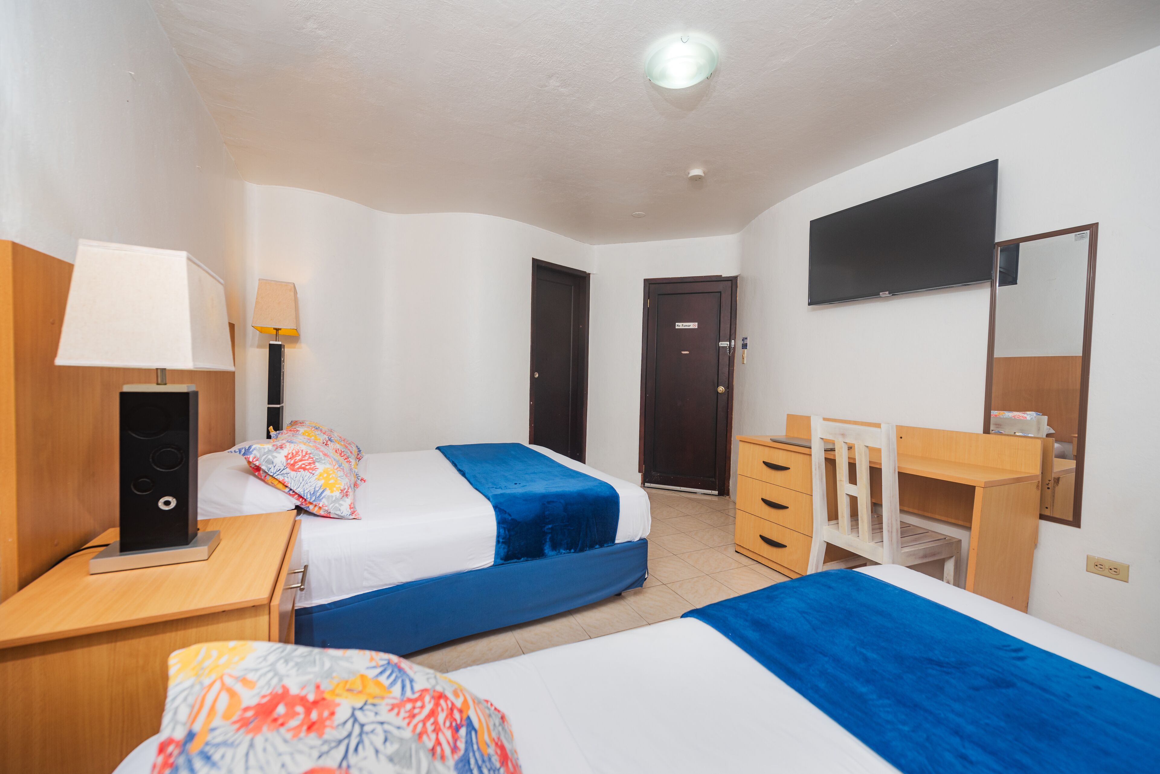 A hotel room with two beds, a desk, a chair, a TV, and a wardrobe.