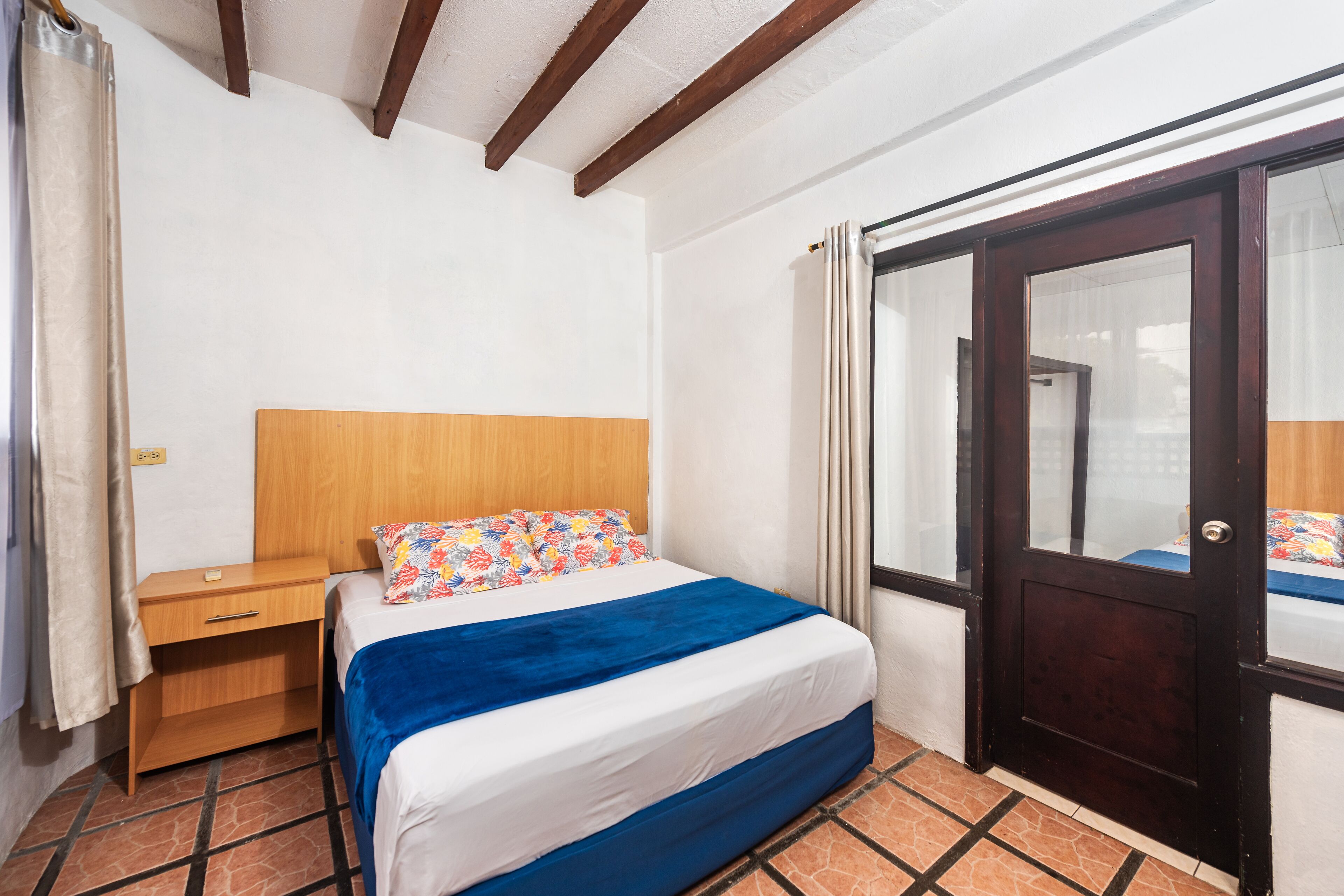 Un dormitorio con cama, mesita de noche de madera y una puerta con panel de vidrio.