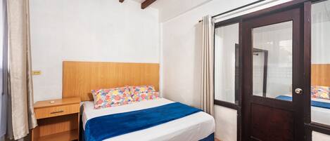 Un dormitorio con cama, mesita de noche de madera y una puerta con panel de vidrio.